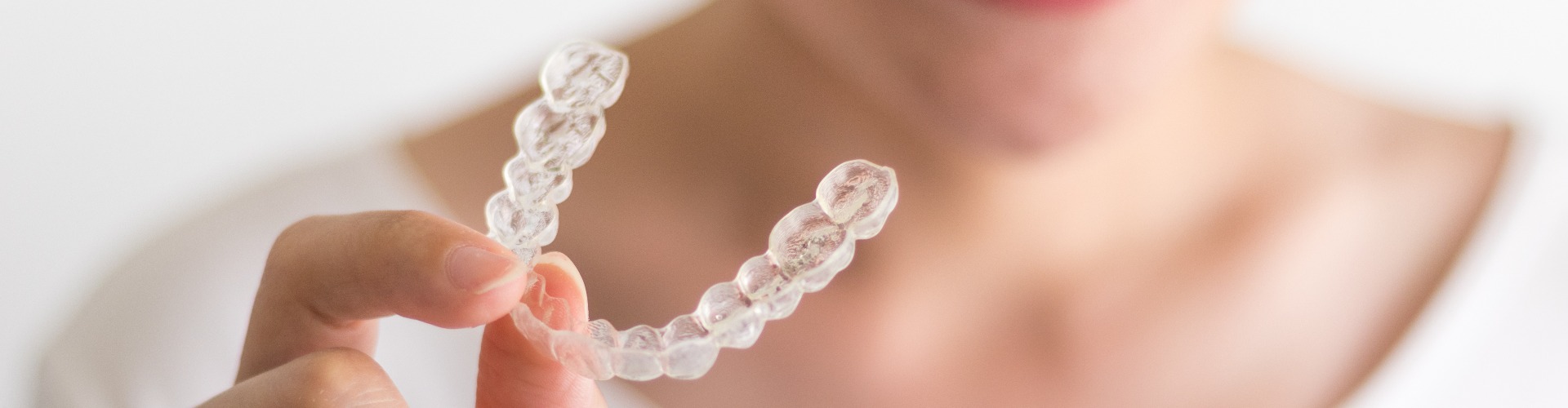 A smiling woman holding invisalign or invisible braces, orthodontic equipment