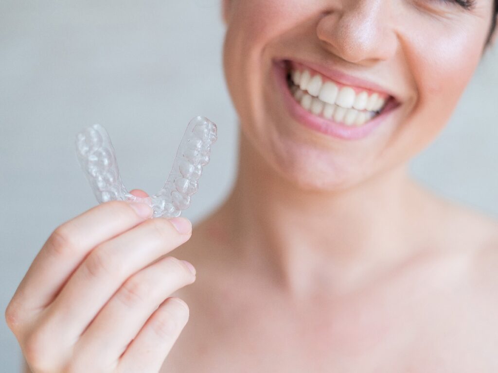 Close-up of orthodontic silicone transparent teeth aligner in female hands. A woman with a perfect charm smile holds a removable night retainer. Bracket for teeth whitening. Cropped photo.