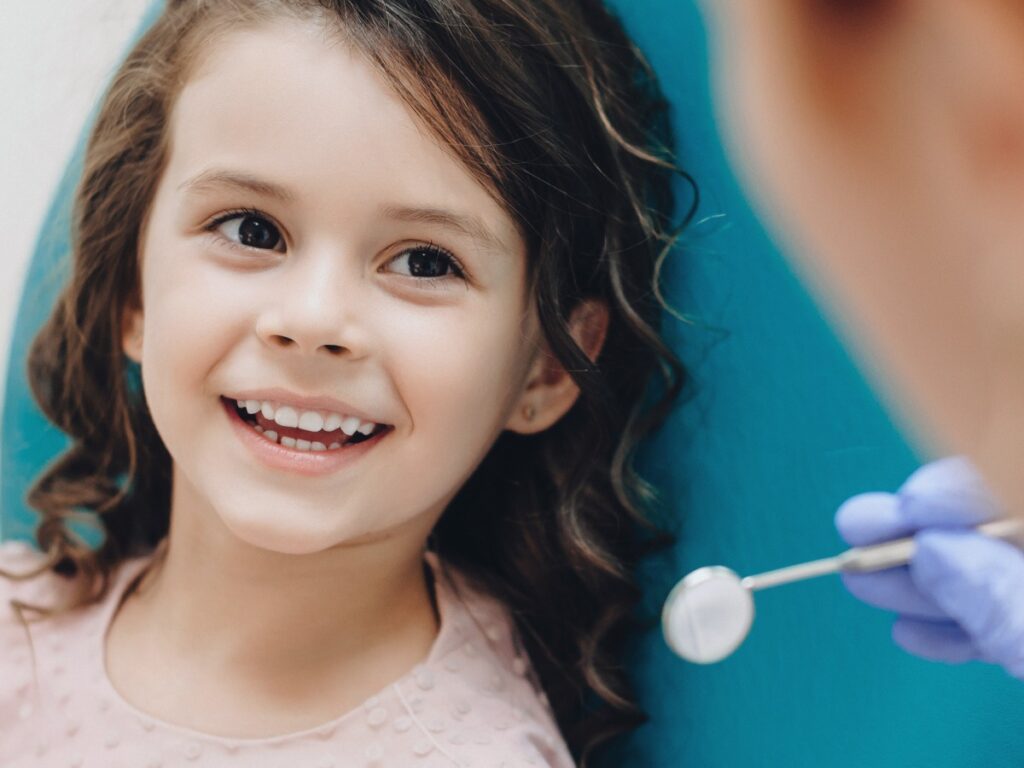 Curly haired little girl looking and smiling to the dentist after a checking up