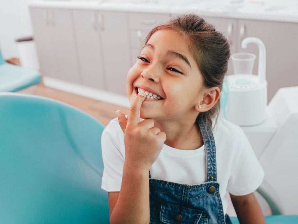 Mixed race little patient showing her perfect toothy smile while sitting dentists chair