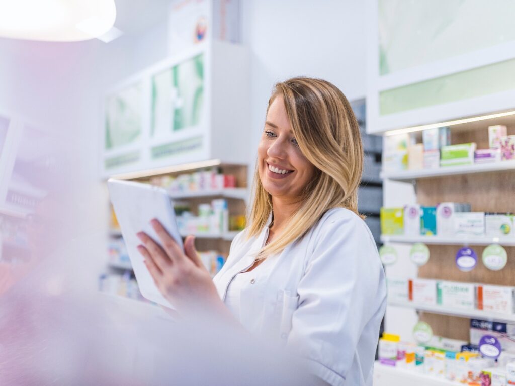 Pharmacist working with a tablet computer in the pharmacy holding it in her hand while reading information