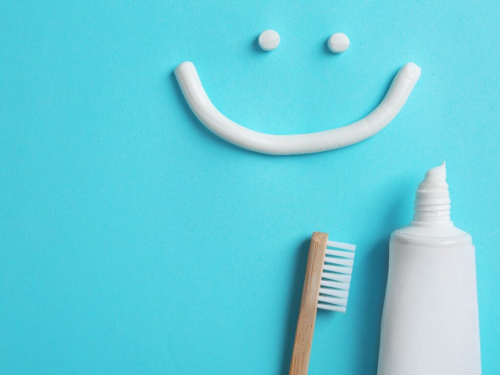 Smiling face made of toothpaste, tube, brush and space for text on color background, top view