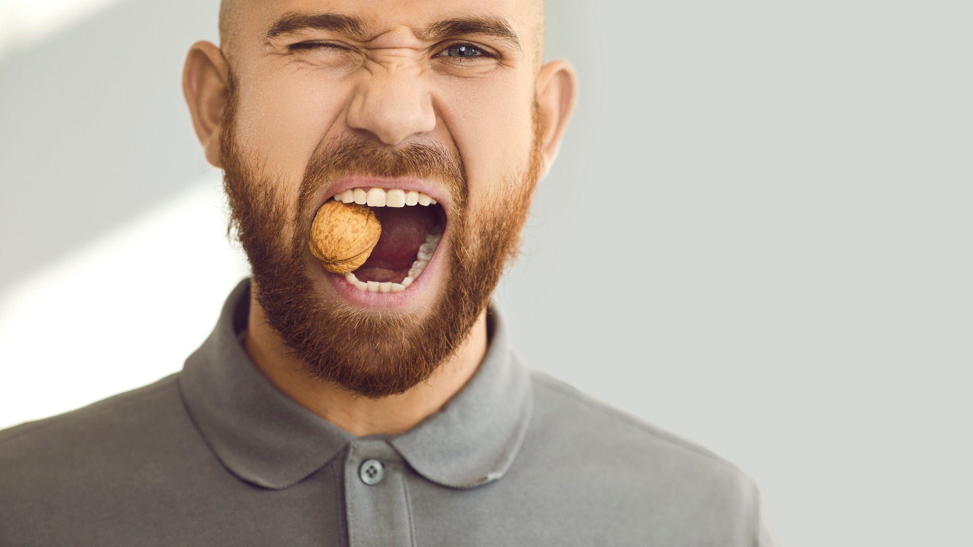 Porträt eines jungen Mannes mit gesunden Zähnen, der versucht, eine harte Walnuss zu knacken